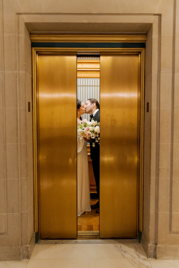 Newlyweds kissing as the brass elevator doors close at San Francisco City Hall.