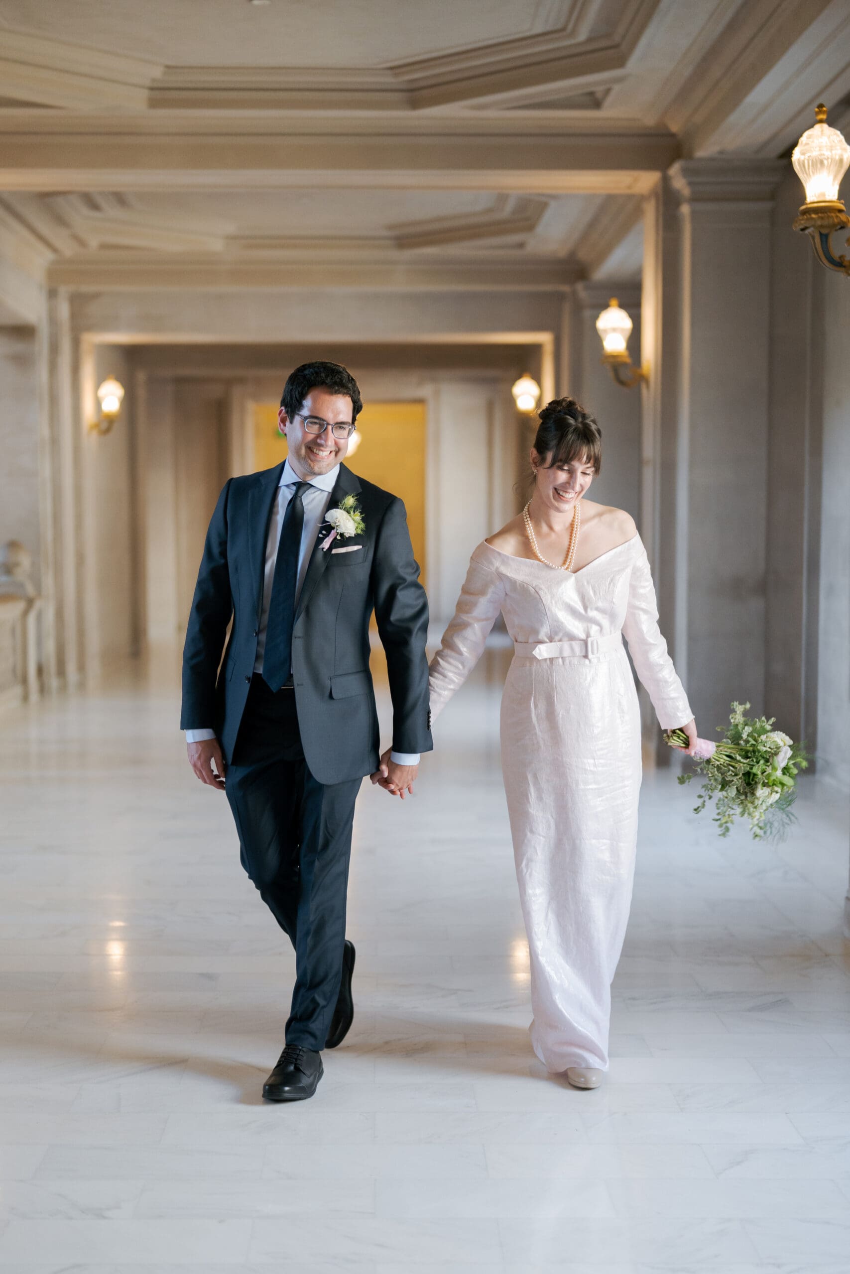Modern couple in chic attire walking through the historic corridors for their San Francisco City Hall elopement.