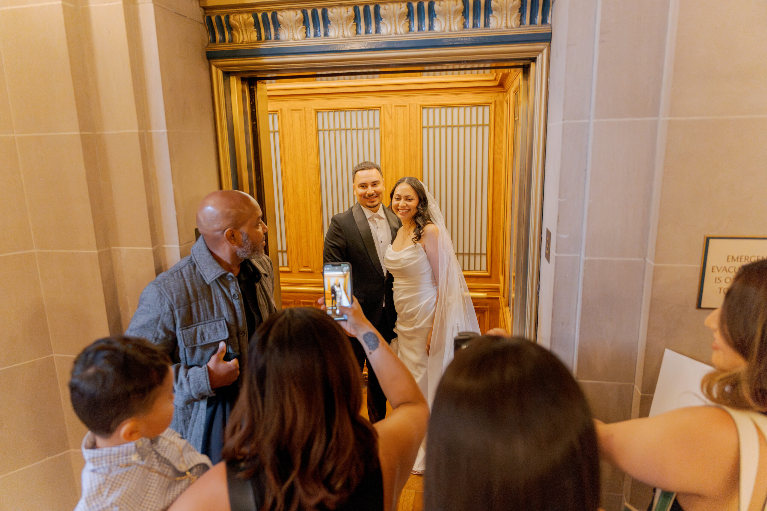 Family and guests gathered outside the ornate elevators of City Hall, showcasing the documentary style of a San Francisco City Hall wedding photographer.
