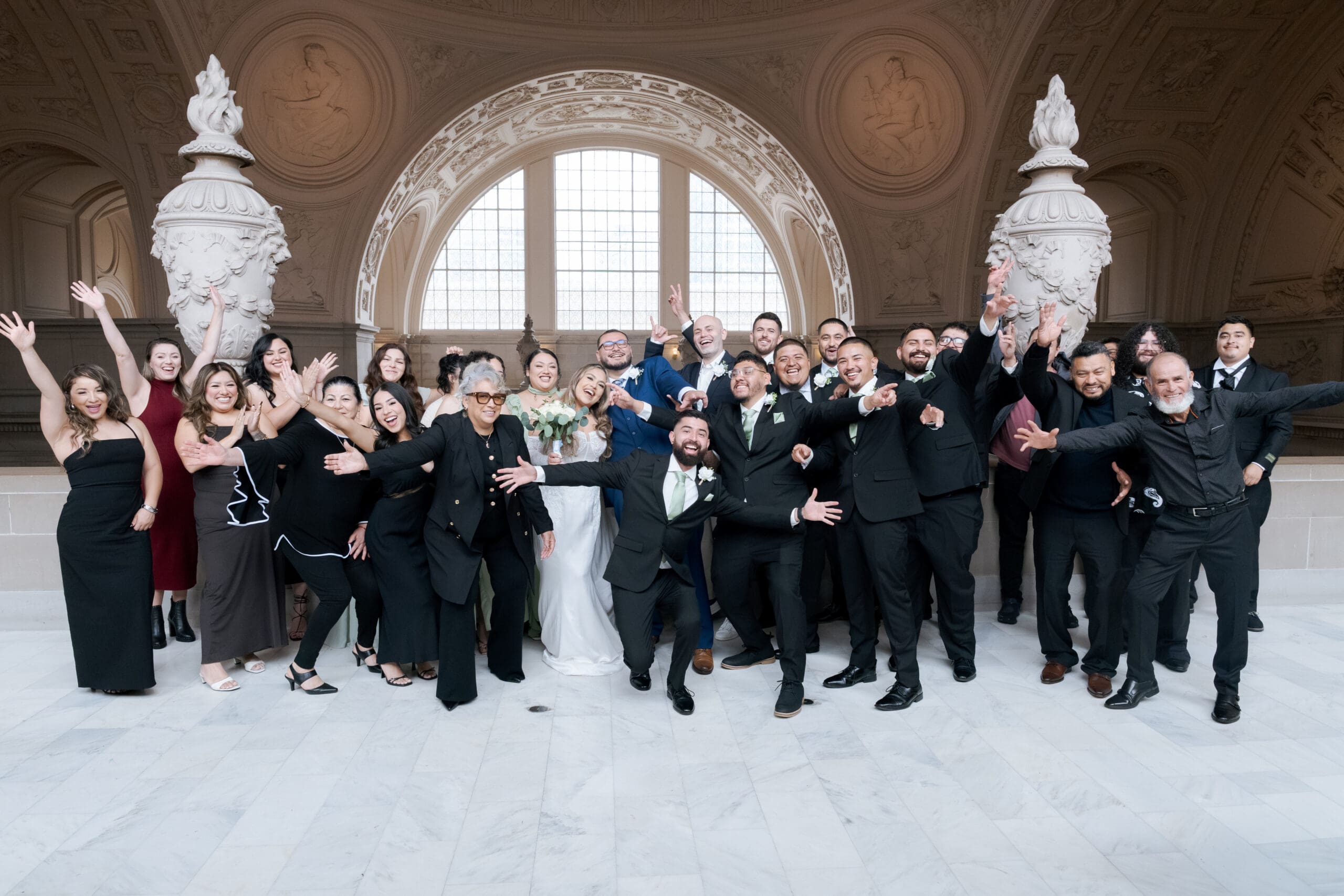 Newlyweds posing for elopement portraits with family and friends in the soft natural light of the 4th Floor North Gallery at San Francisco City Hall.