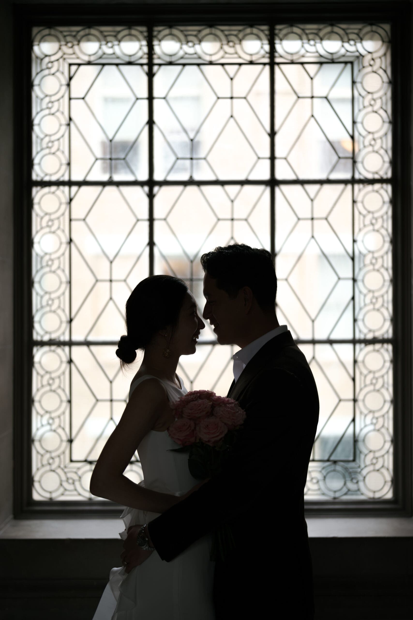 Silhouette of a newlywed couple framed against the historic City Hall windows.