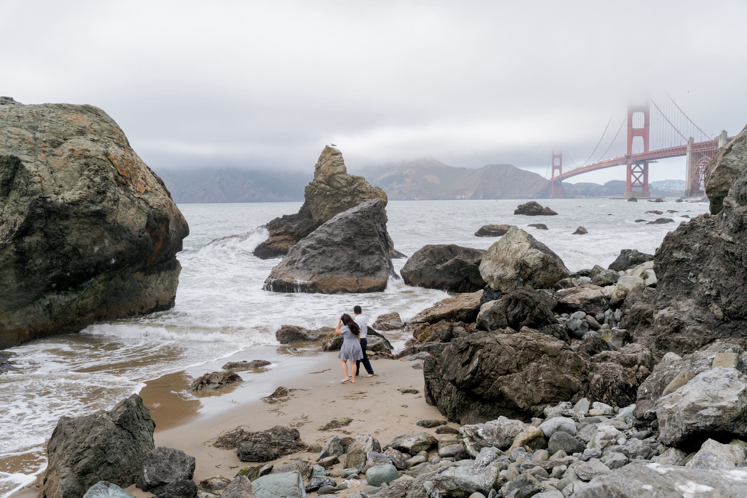 Engaged Couple during their engagement photoshoot at San Francisco's Marshall's Beach with the Golden Gate Bridge in the background