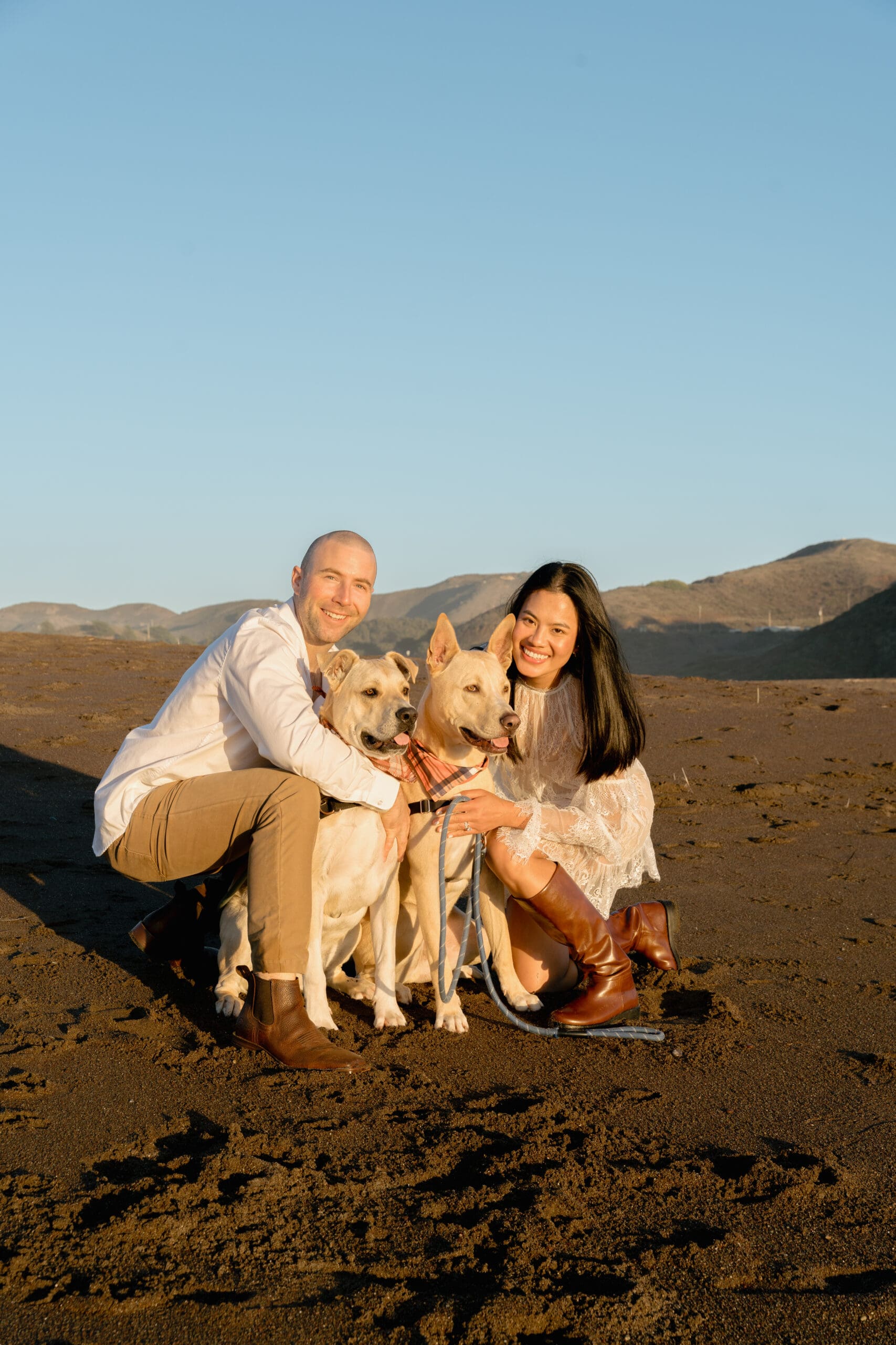 Happy couple and their two dogs during engagement  photo session on the beach at sunset