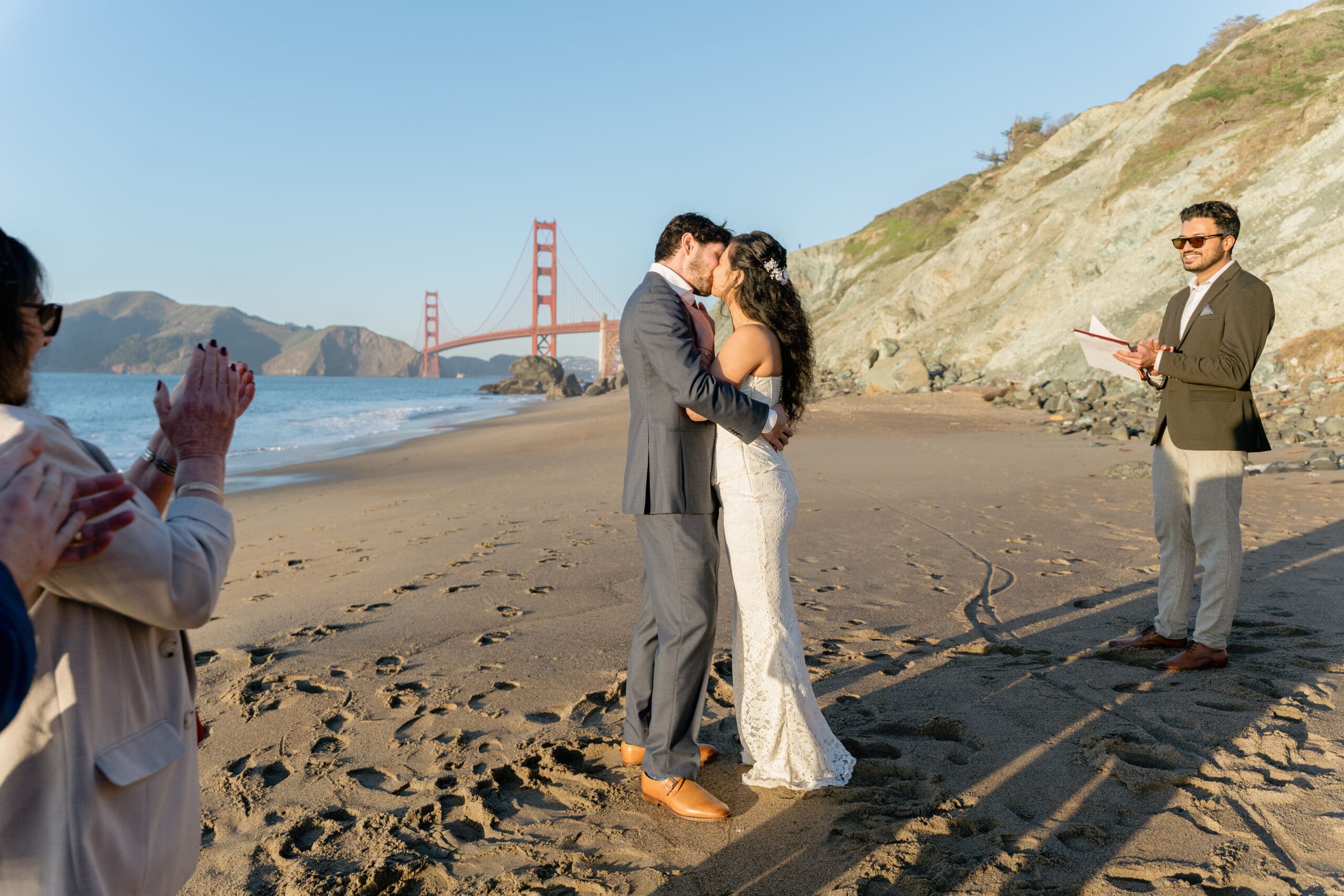 A first kiss between newlyweds on San Francisco's Marshall's Beach during golden hour, with the Golden Gate Bridge in the background