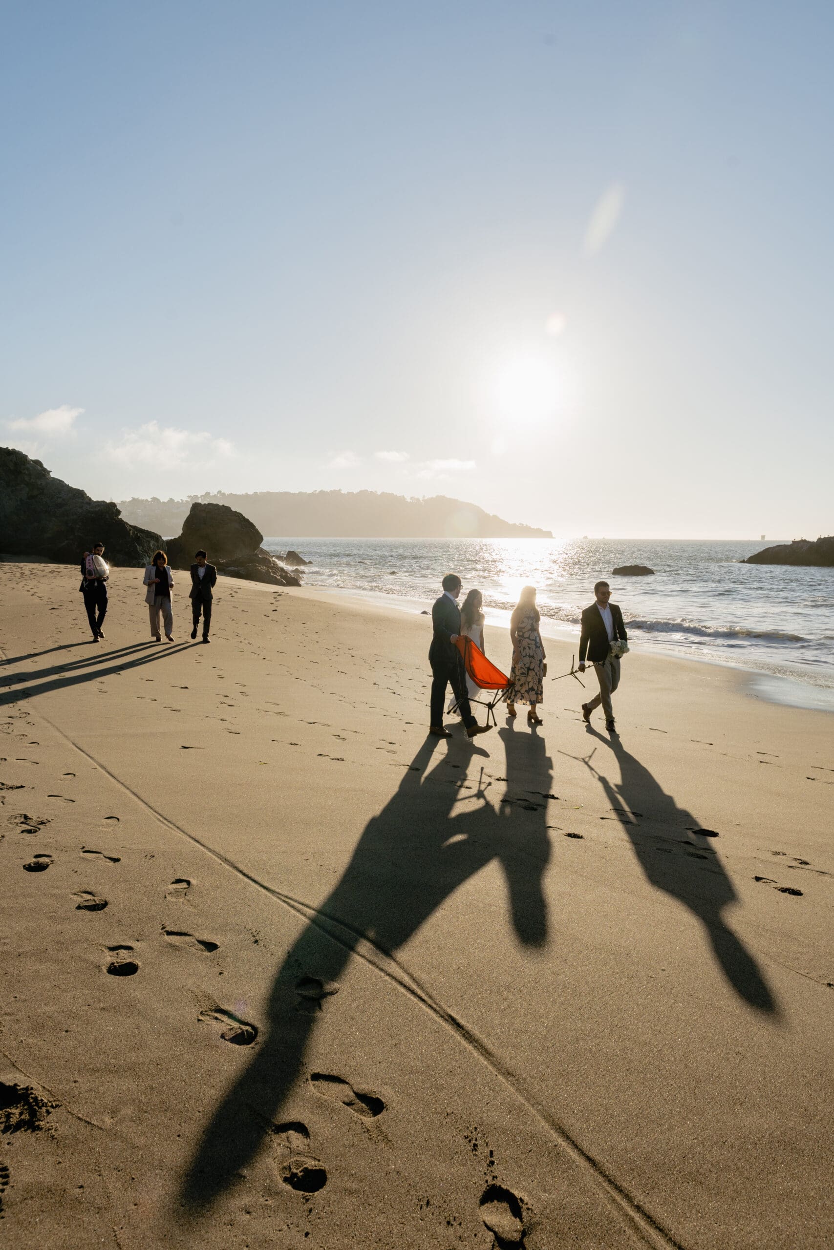 Friends and family gather for the elopement ceremony on Marshall's Beach during golden hour sunset