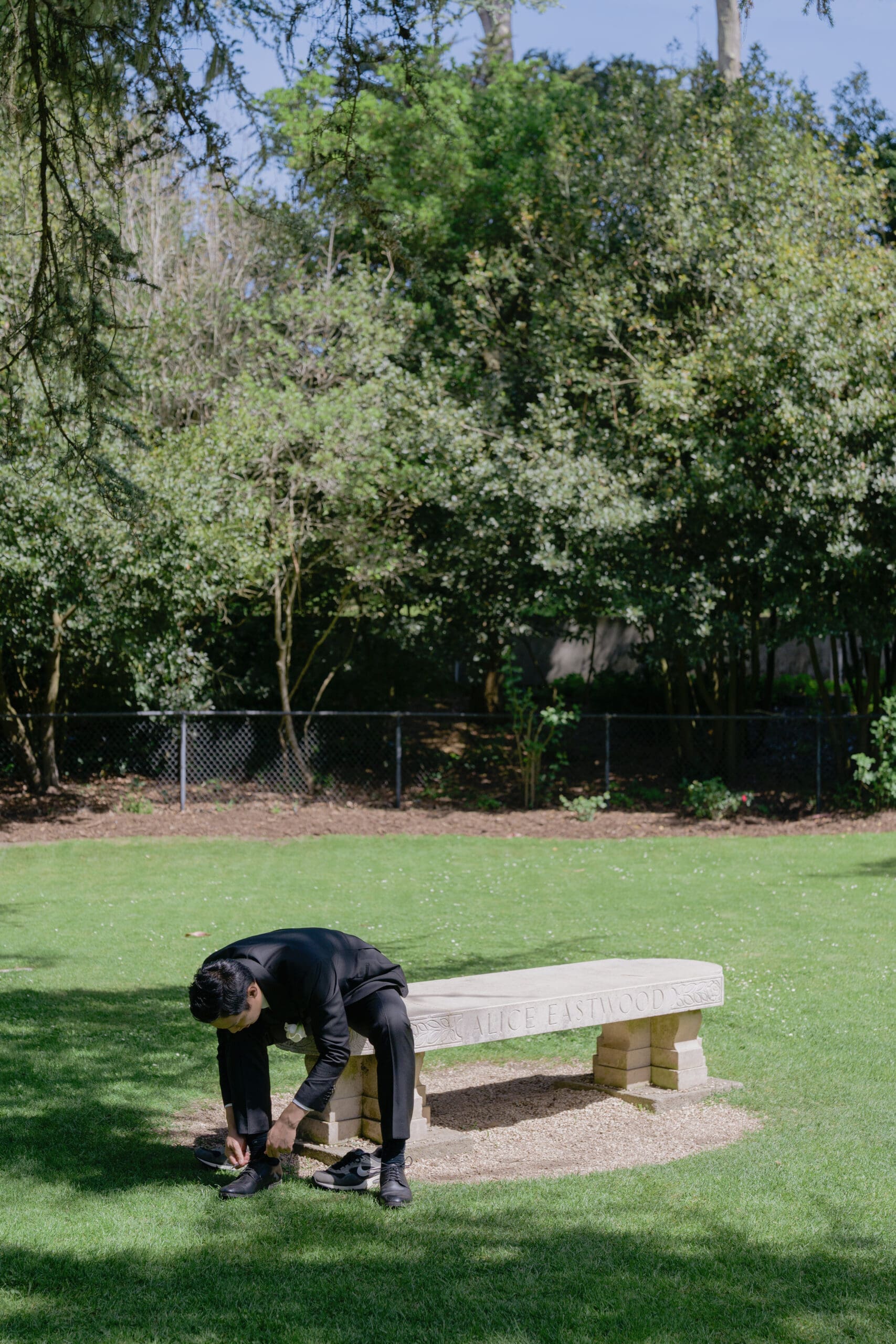 A groom does his final prep on bench within the Shakespeare Garden before the intimate wedding ceremony